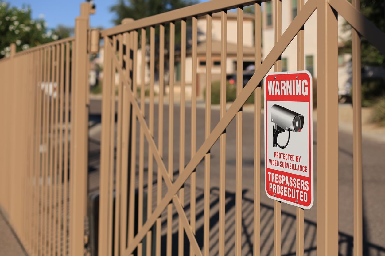 Trespassers Prosecuted warning sign placed on the bars of metal fence in a city residential housing gated community