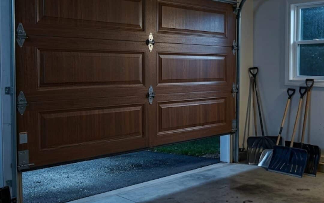 Inside a home garage at night with a broken torsion spring above a wood-grain garage door, illustrating an urgent mechanical failure.