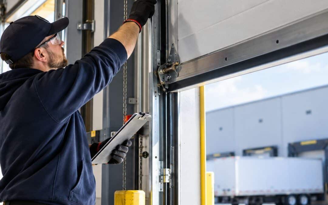 Technician inspecting a commercial overhead garage door during routine maintenance at a warehouse loading dock.